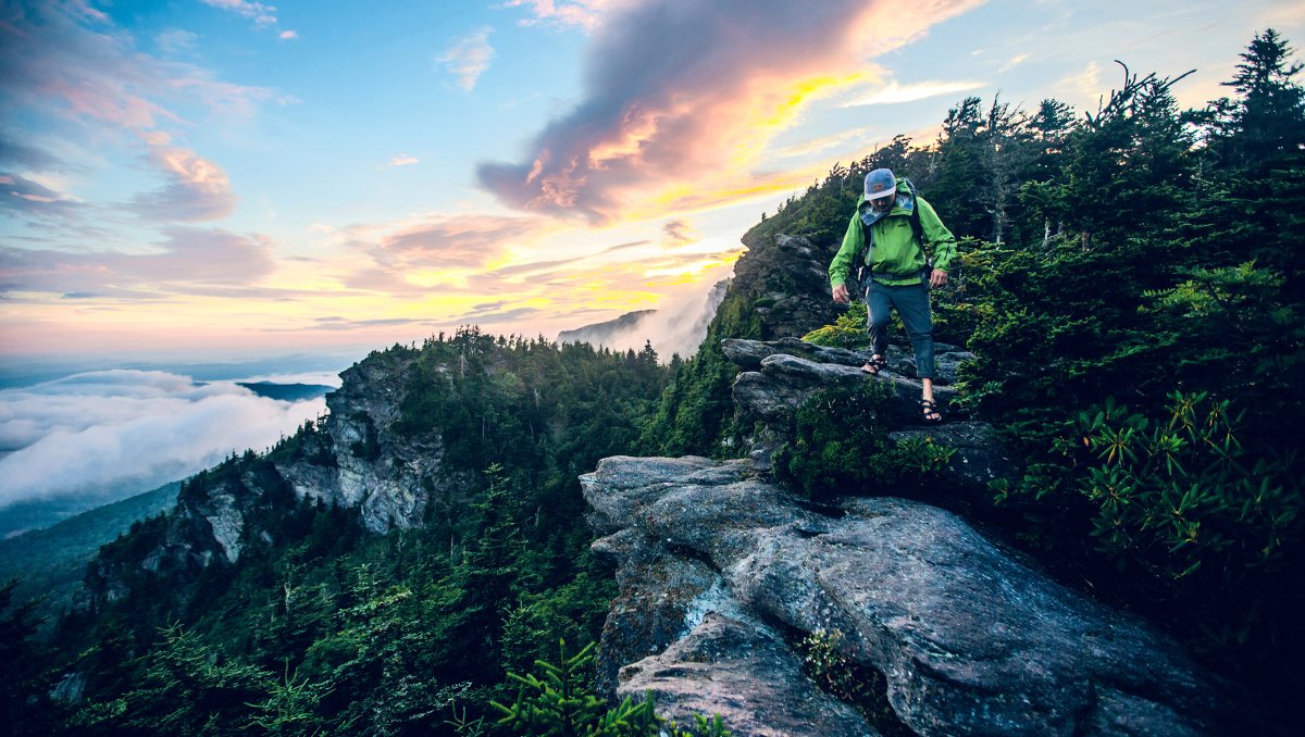 Person hiking down from peak of mountain surrounded by trees and views