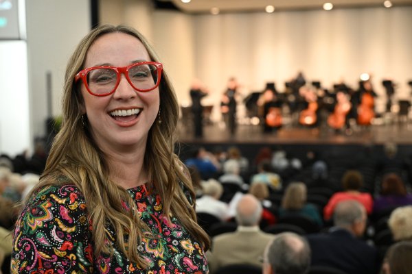 Woman smiling at camera with symphony on stage in background