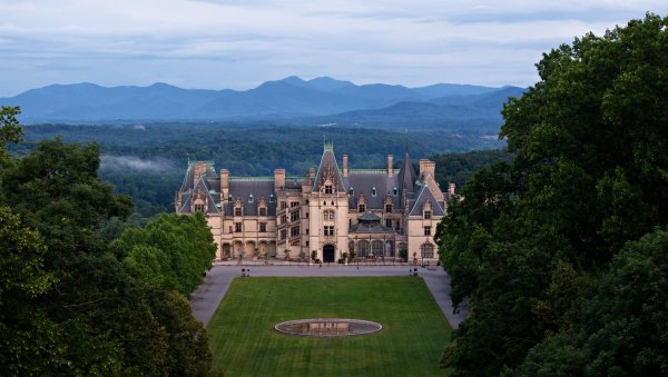 Aerial of Biltmore House and grounds with Blue Ridge Mountains rising in background.
