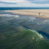 Person fishing from shore on empty beach.