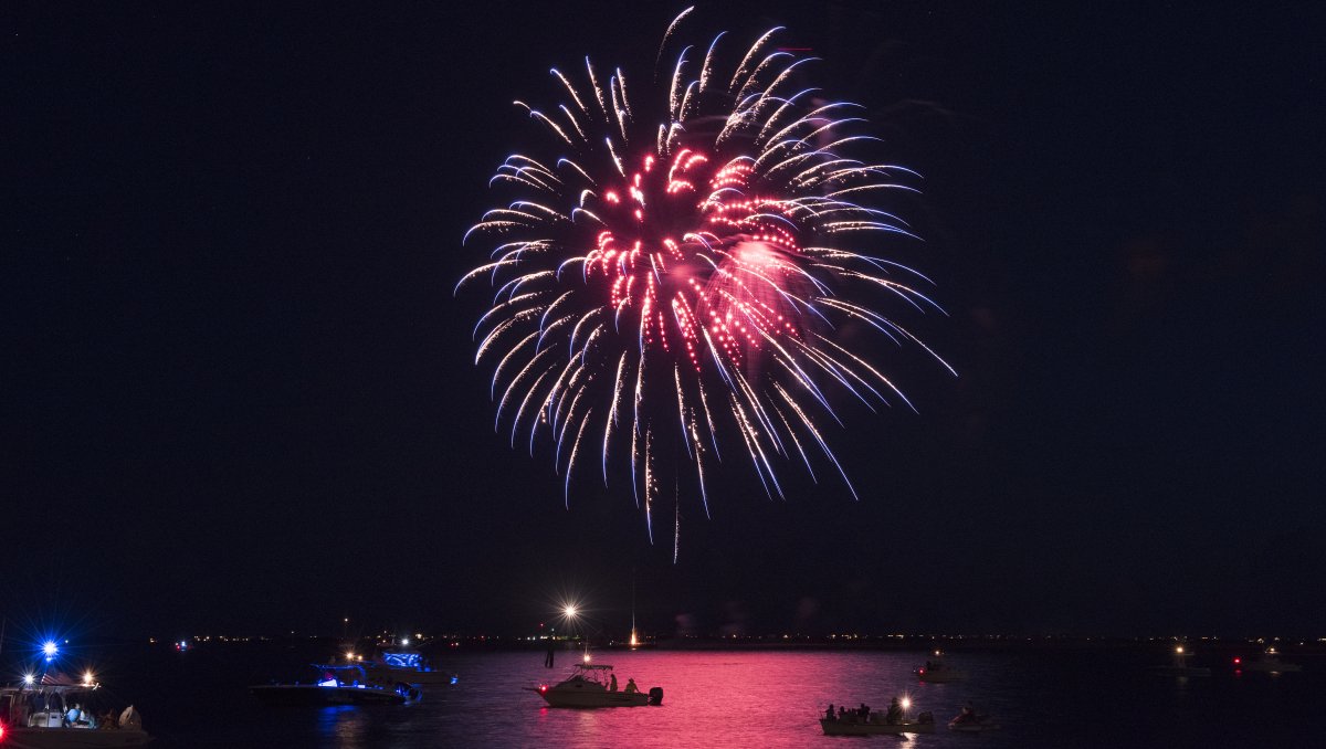 Fireworks exploding in night sky with boats floating in water below.