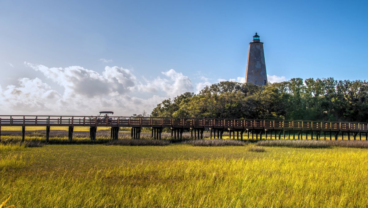 Marsh and wood bridge on Bald Head Island with Old Baldy Lighthouse in distance.