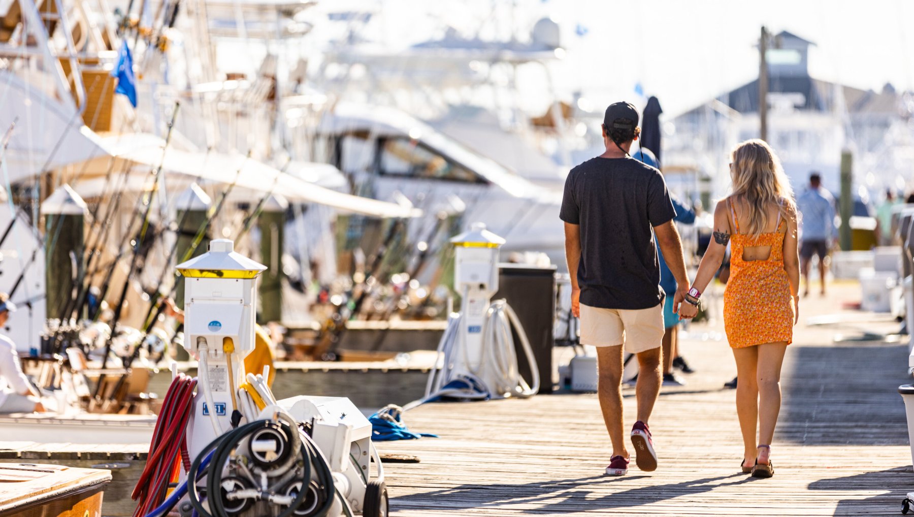 Couple holding hands while walking on docks with large fishing boats lined up to left