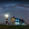 Bodie Island Lighthouse shining brightly at night under starry sky.