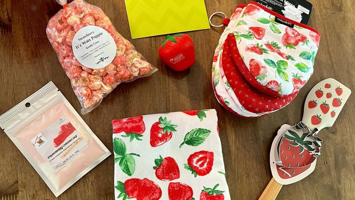 A vibrant red bag filled with strawberries, accompanied by a spoon, knife, and a colorful bag of candy.