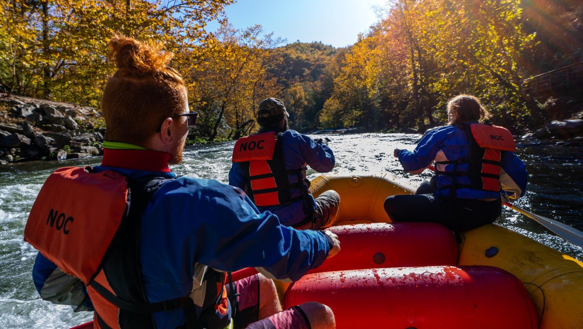 Three paddlers whitewater rafting down river surrounded by fall foliage