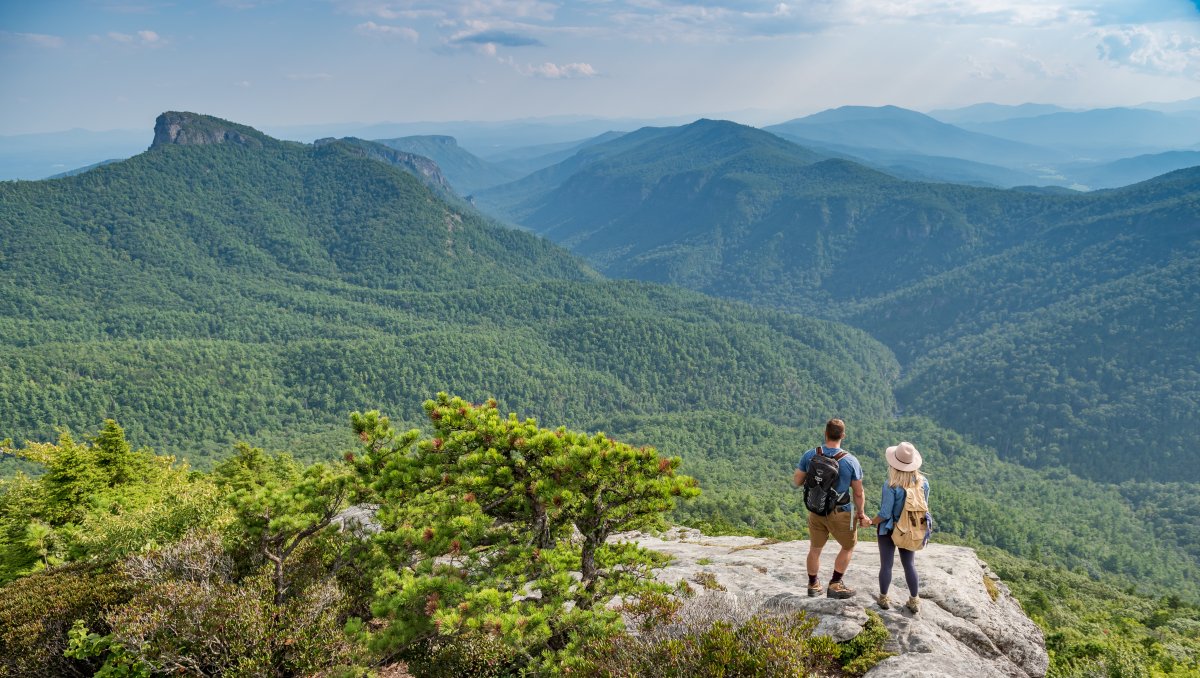 Couple standing on Hawksbill Mountain summit, looking out at mountain vistas.
