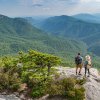 Couple standing on Hawksbill Mountain summit, looking out at mountain vistas.