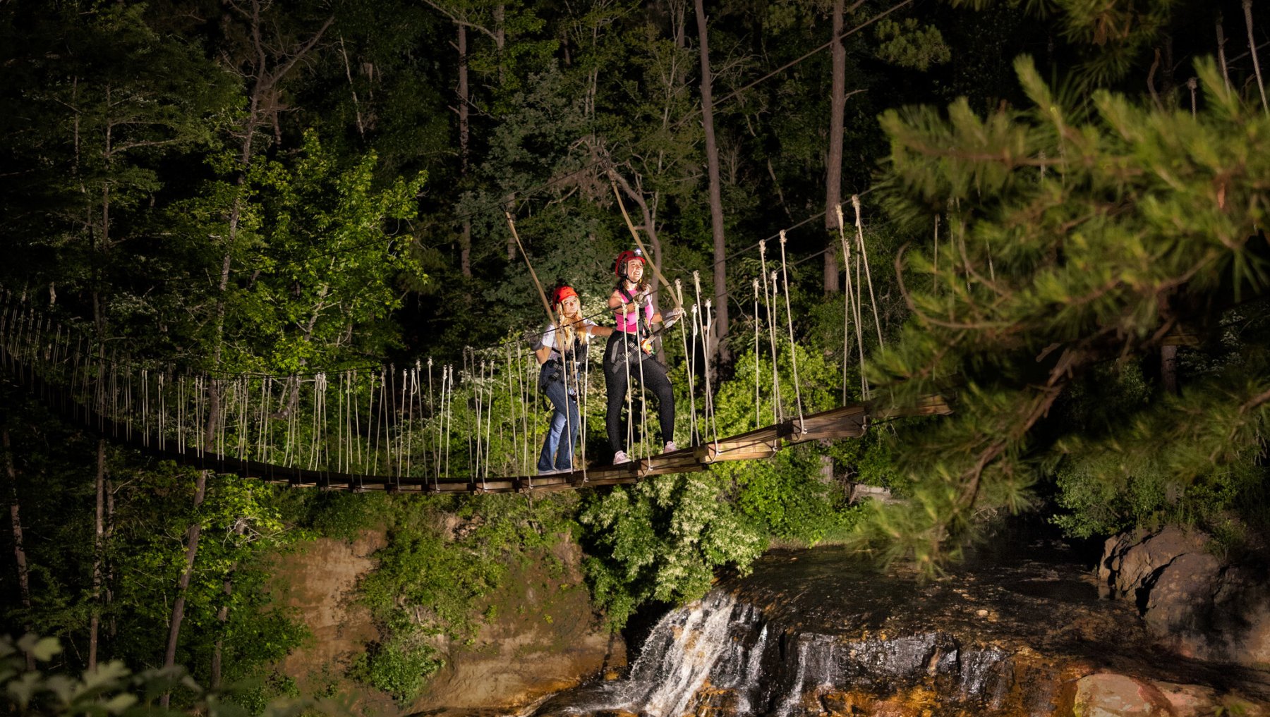 Two friends walking across drawbridge over waterfall at night at ZipQuest.