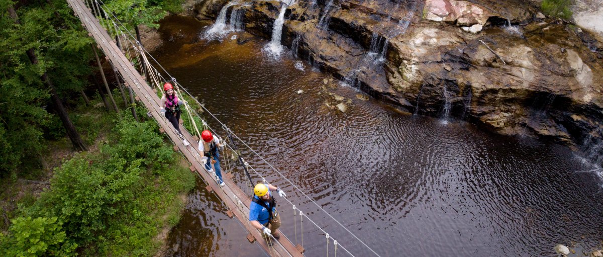 People walking on drawbridge over waterfalls and creek.