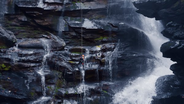 Person rappelling down Big Bradley Falls as water rushes down around them.
