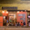 People sitting outside at tables at Fullsteam Brewing at nighttime.