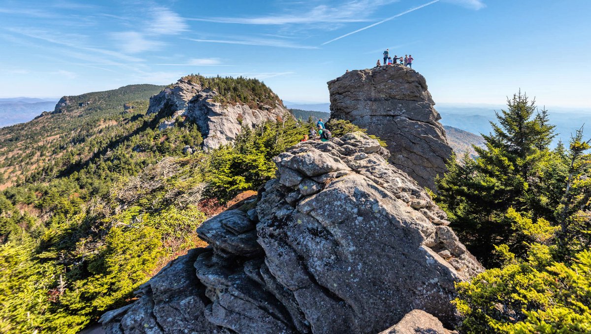 People standing on mountaintop in distance, surrounded by other peaks
