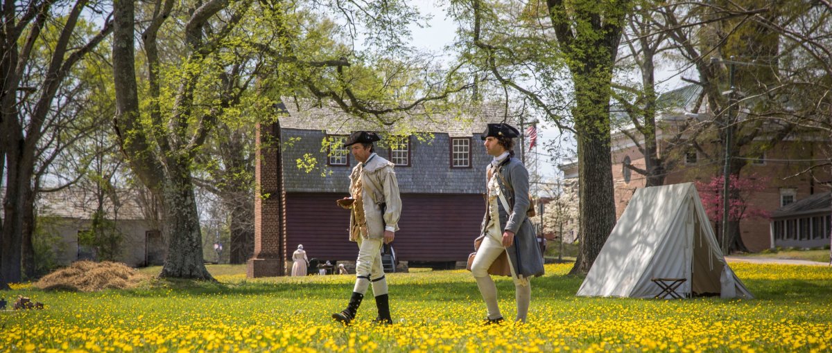 Revolutionary War re-enactors walking on Halifax grounds with historic buildings in background.