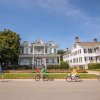 Group of four on bikes touring historic neighborhood with beautiful home in background.