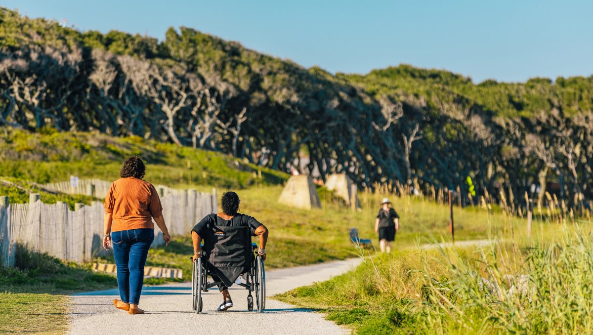 Friends, one in a wheelchair, exploring Fort Fisher on accessible path.