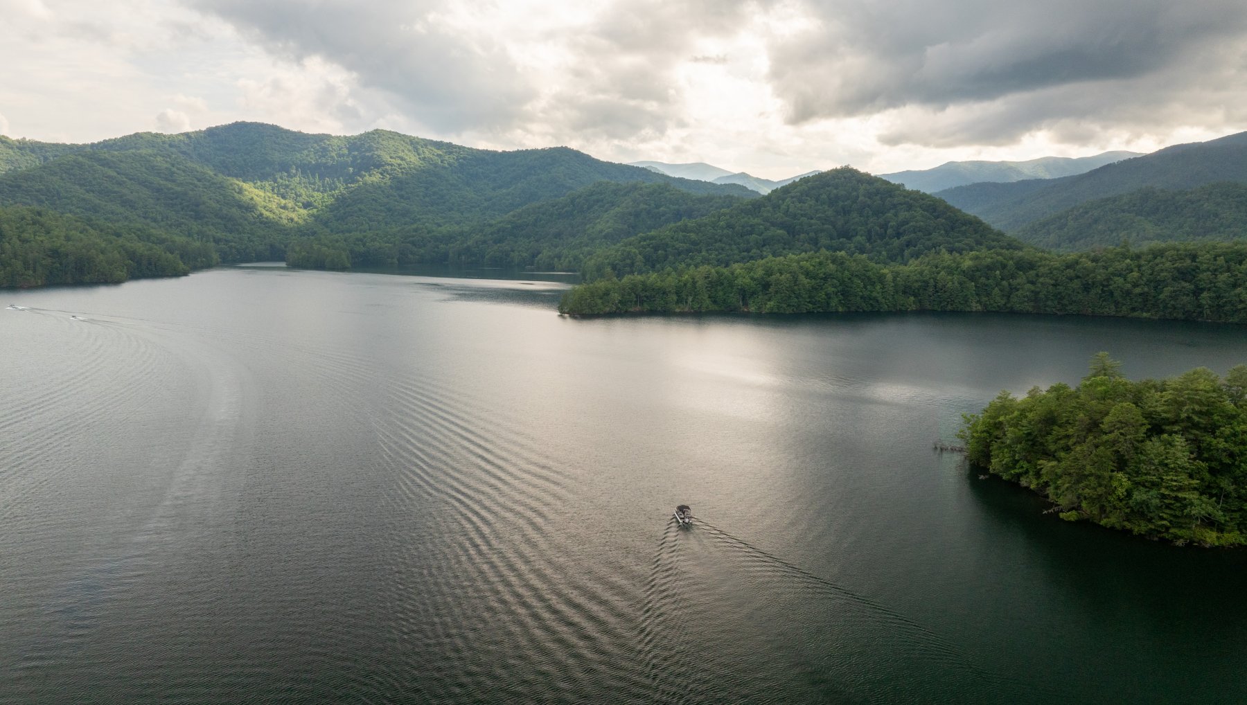 Aerial of boat driving through calm Lake Santeetlah, surrounded by mountains.