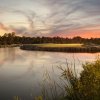 Golf course greens sitting on body of water under beautiful pink and blue sky.