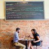 Couple sitting at table at tapas restaurant with brick wall behind them.