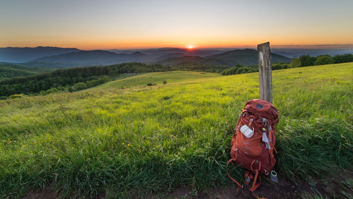 Backpack sitting against wooden post with sun rising over Appalachian Mountains at sunrise.