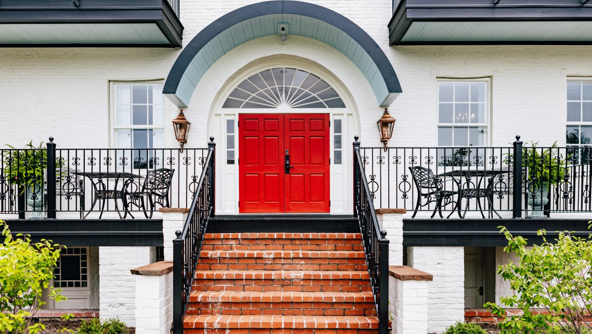 Exterior of white mansion inn with bright red door and brick steps leading to landing