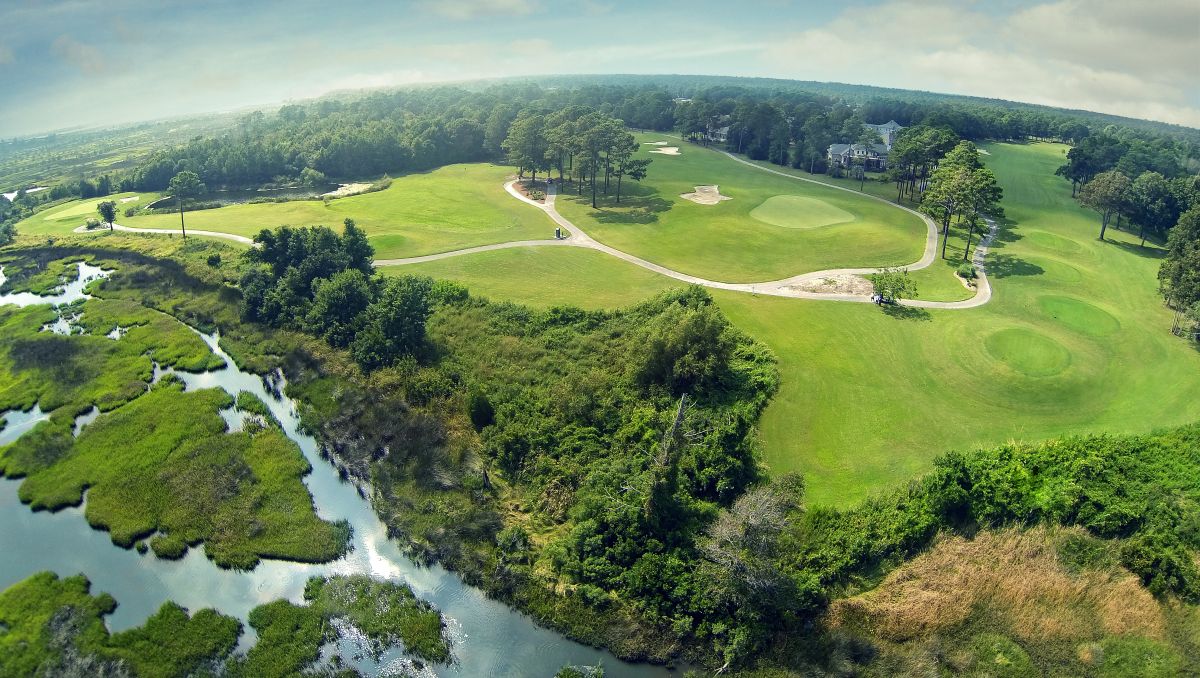 Aerial view of golf course greens, trees, marshes and cart paths on bright day