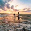 Two people surf cast fishing at sunset in Ocracoke, NC.