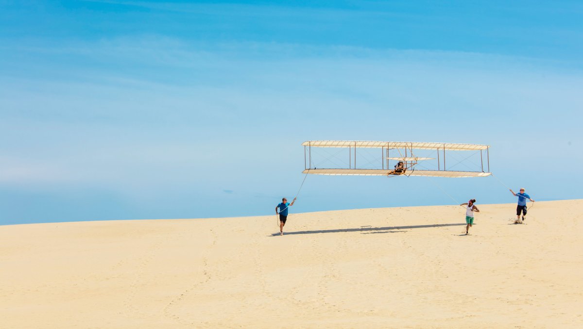 People assisting in getting hang glider off the ground on sand dune.