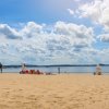 Sandy beach with lifeguard and visitors sitting in front of lake during summer day.