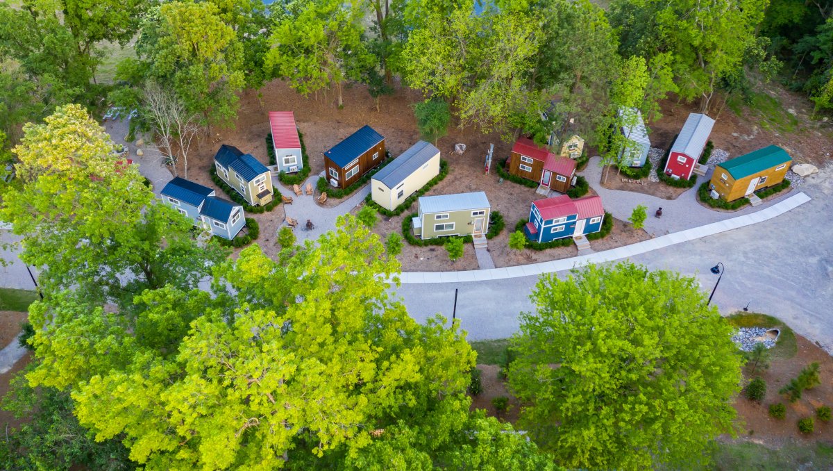 Aerial shot of tiny houses making up tiny house hotel, surrounded by tall bright green trees during daytime