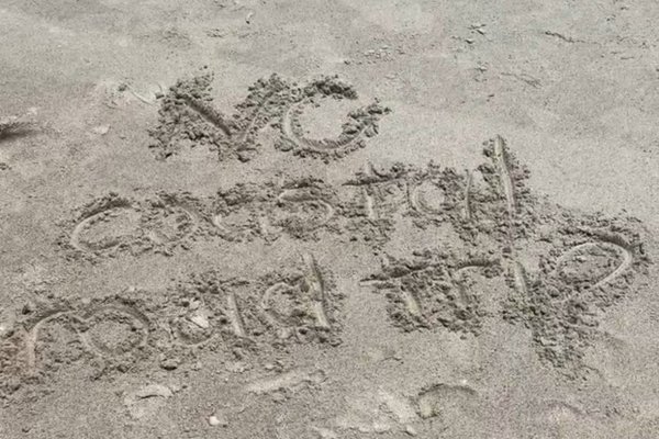 "NC Coastal Road Trip" written in sand on Southport, NC, beach.