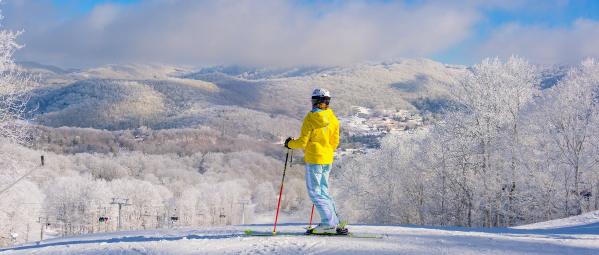 Skiier standing at top of slope looking out over snowy mountains during daytime.