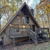 Woman sitting on front steps on A-frame home in woods.